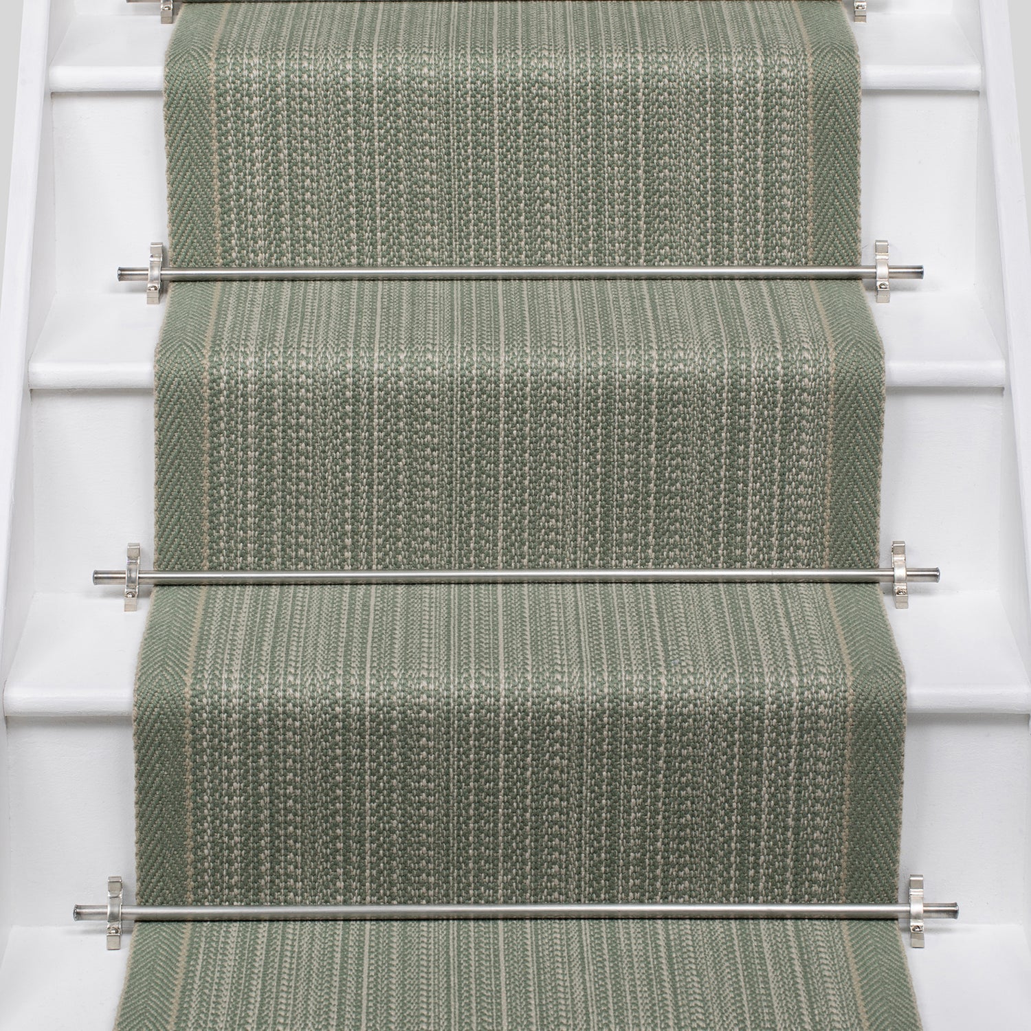 A textured stair runner in a muted sage green color installed on a white staircase, secured by silver metal rods.