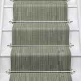 A textured stair runner in a muted sage green color installed on a white staircase, secured by silver metal rods.