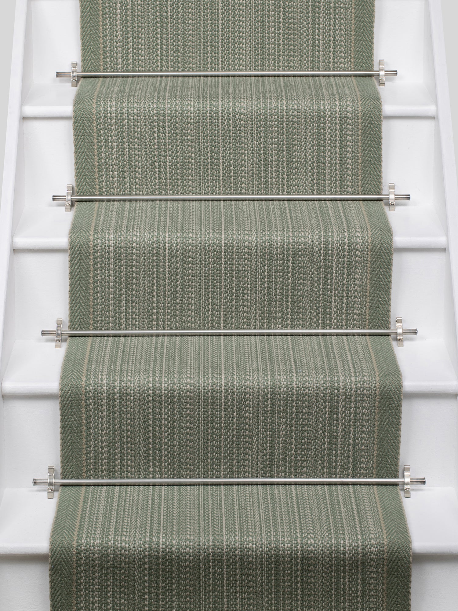 A textured stair runner in a muted sage green color installed on a white staircase, secured by silver metal rods.