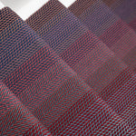 A close-up of stair runner with a woven herringbone pattern in dark red, burgundy, and navy tones.