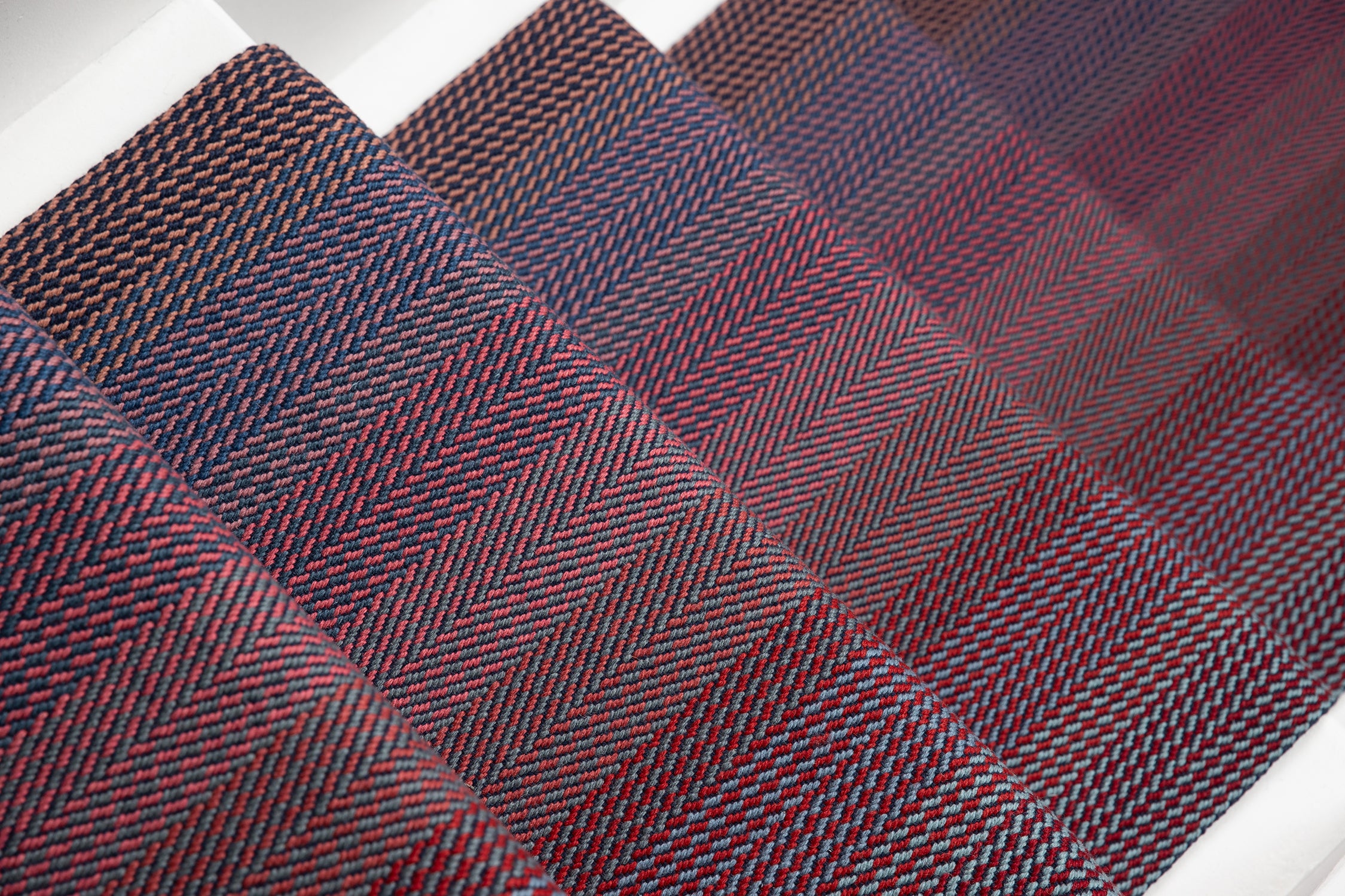 A close-up of stair runner with a woven herringbone pattern in dark red, burgundy, and navy tones.