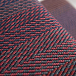 Close-up of a stair runner with a herringbone pattern in red and dark gray, showing the texture and weave detail.