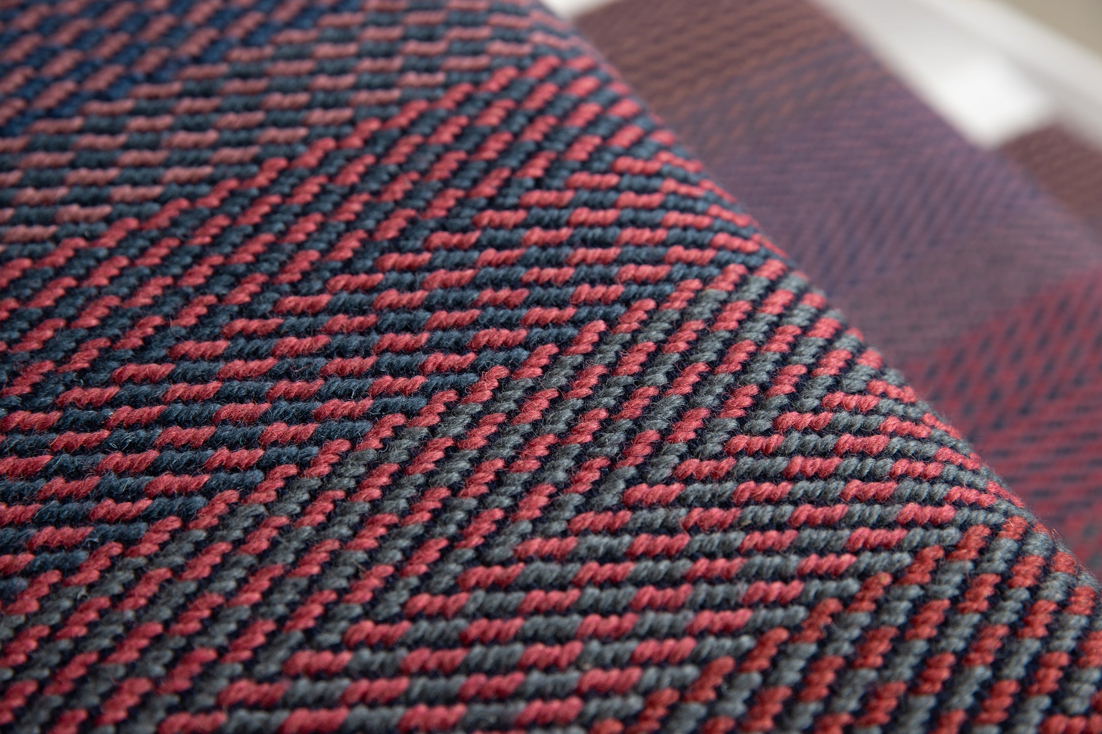 Close-up of a stair runner with a herringbone pattern in red and dark gray, showing the texture and weave detail.