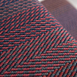 Close-up of a stair runner with a herringbone pattern in red and dark gray, showing the texture and weave detail.