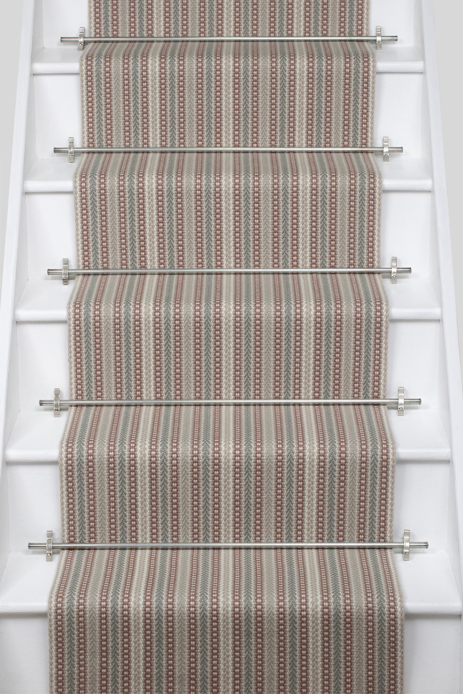 White stair case with a runner in a complex woven stripe design of wool in shades of pink and grey.