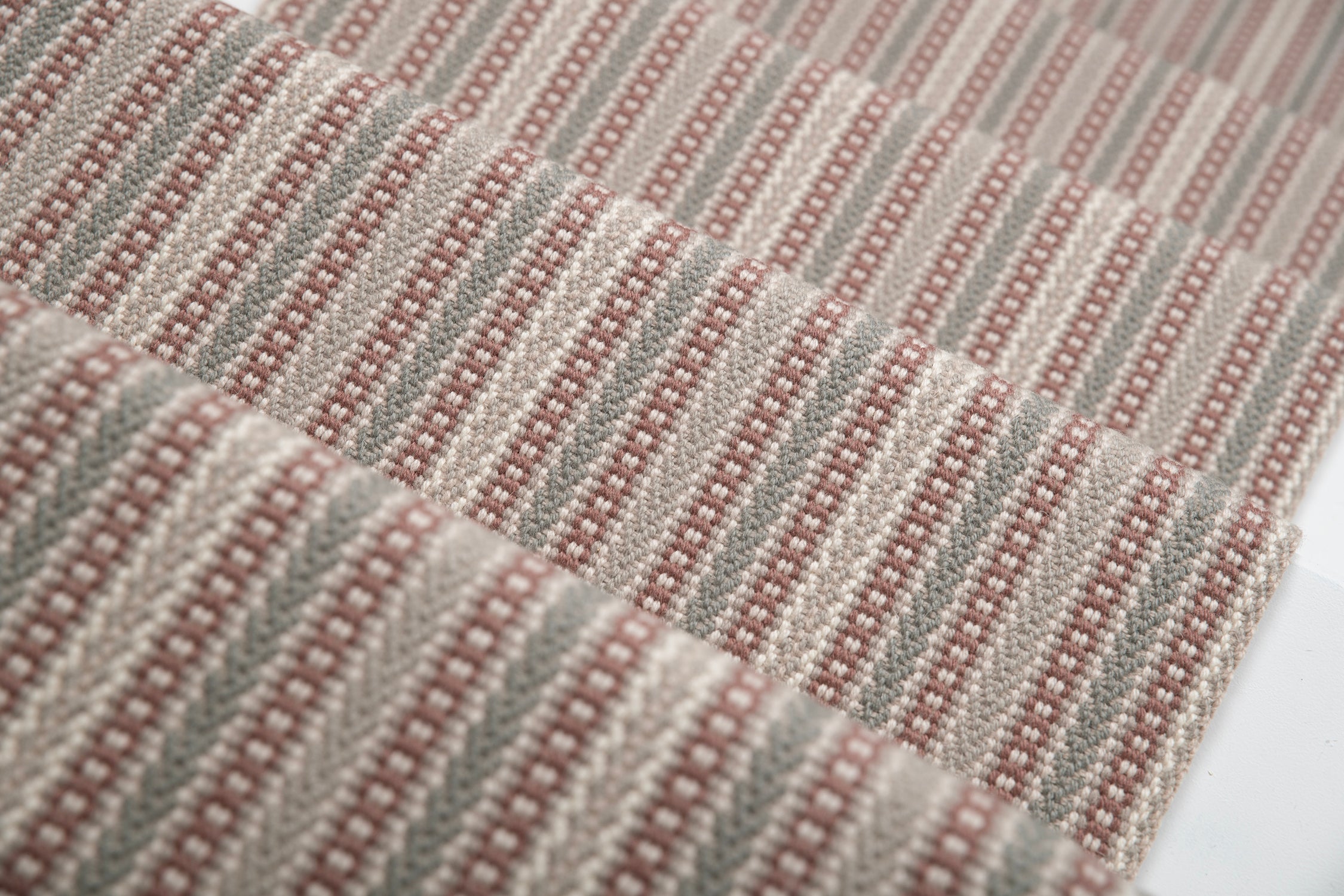 Detail of a stair runner in a complex woven stripe design of wool in shades of pink and grey.