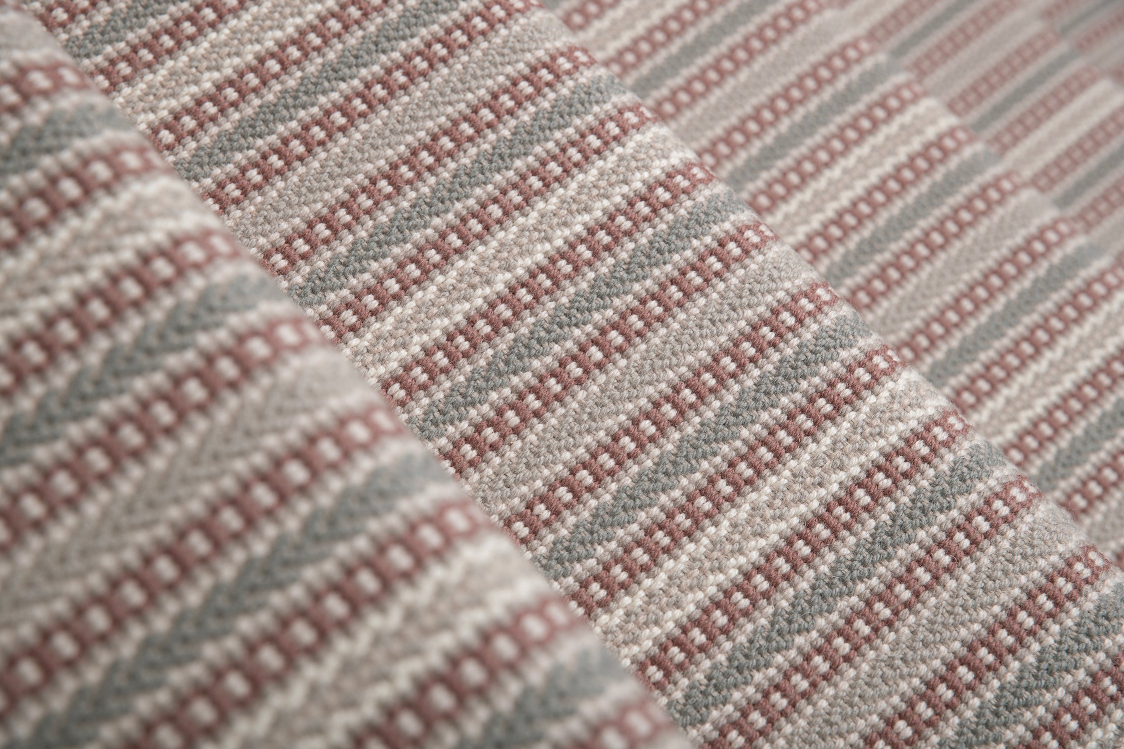 Detail of a stair runner in a complex woven stripe design of wool in shades of pink and grey.