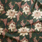 Close up of tropical floral gently draped printed linen featuring cream-colored blossoms with pink centers, dark green leaves on a brick red background.