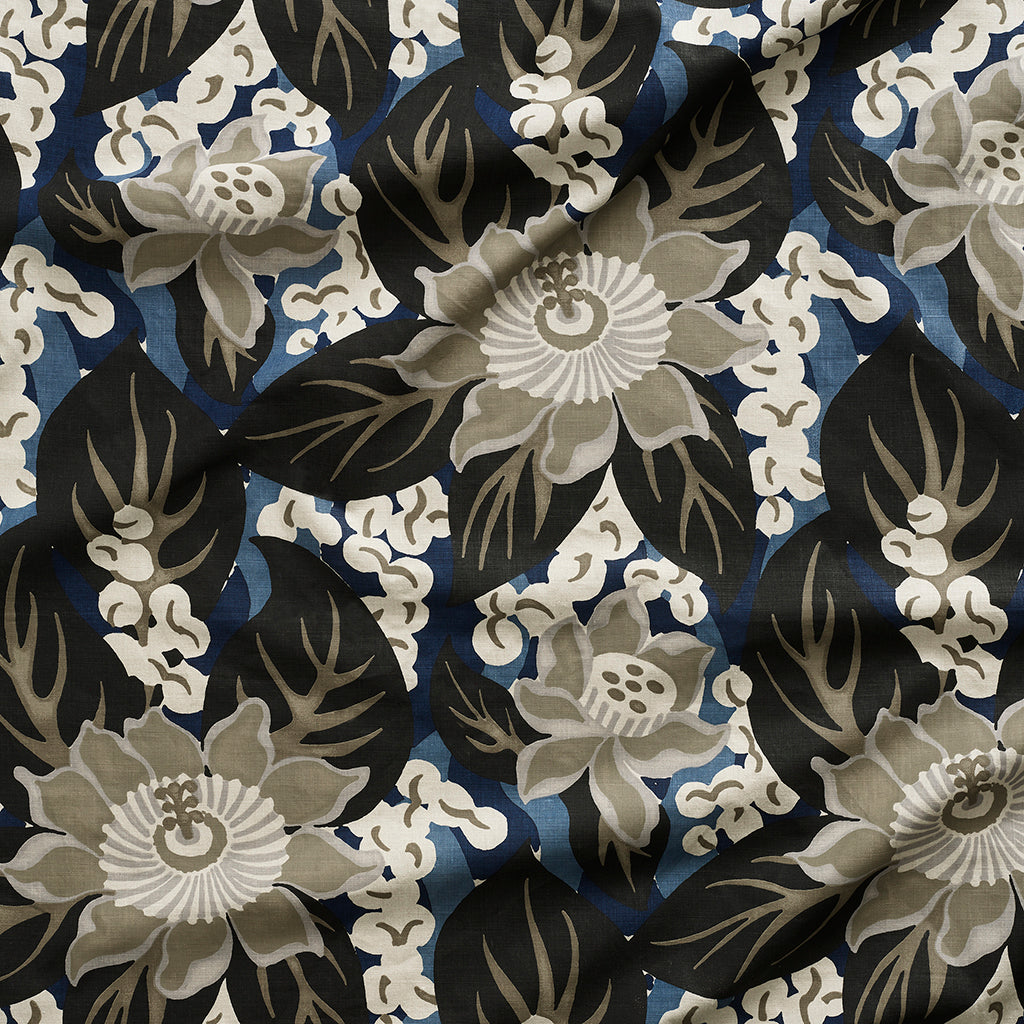 Close up of tropical floral gently draped printed linen featuring pale grey-colored blossoms with taupe centers, black leaves on a blue background.
