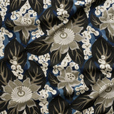 Close up of tropical floral gently draped printed linen featuring pale grey-colored blossoms with taupe centers, black leaves on a blue background.