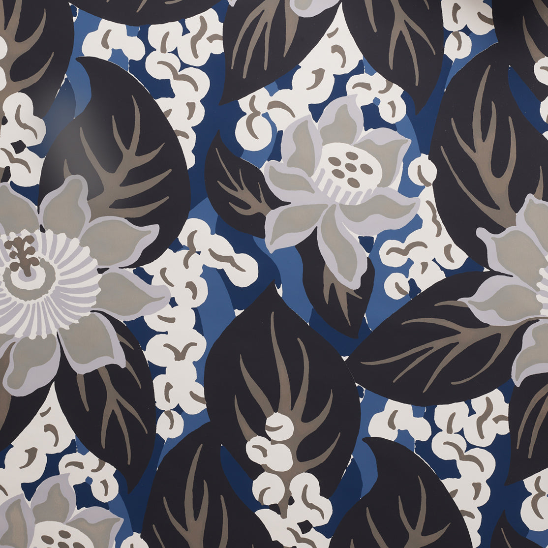 Close up of tropical floral wallpaper featuring grey colored blossoms with cream centers, black leaves on rich blue background. 