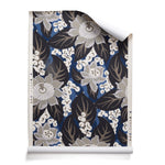 A roll of tropical floral wallpaper featuring grey colored blossoms with cream centers, black leaves on rich blue background. 