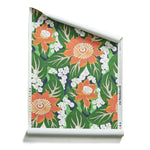 A roll of tropical floral wallpaper featuring orange and yellow flowers with white centers, dark green leaves, and small white lily-of-the-valley style blooms on a dark navy background.