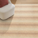 Beige striped rug on a wooden floor with a white chair and red cushion.