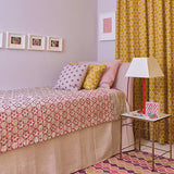 Bedroom with patterned bedspread, yellow curtains, and a side table.