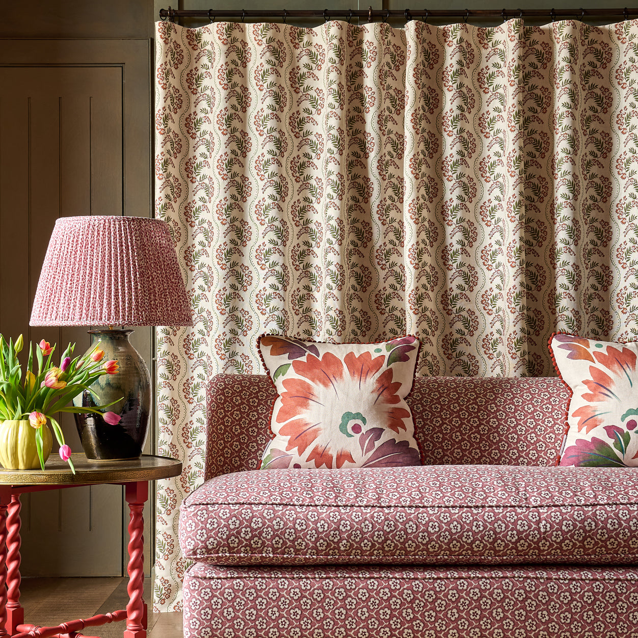 Patterned sofa with decorative pillows in a room with a lamp and floral arrangement.