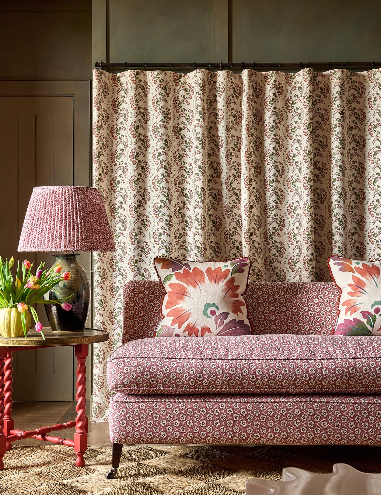 Patterned sofa with decorative pillows in a room with a lamp and floral arrangement.