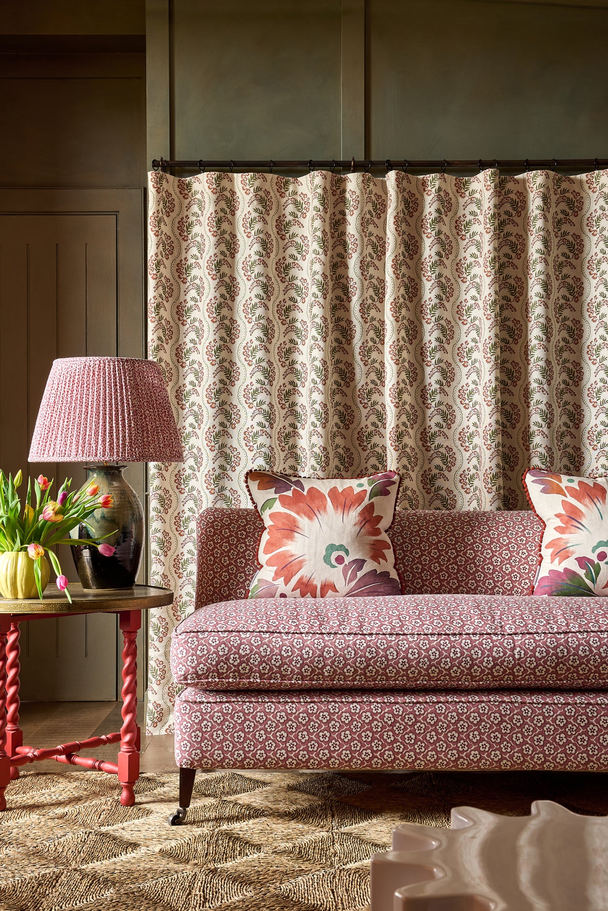 Patterned sofa with decorative pillows in a room with a lamp and floral arrangement.