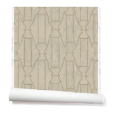 Partially unrolled wallpaper in a repeating curvolinear print in gold on a painted cream field.