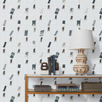 A table with books and a lamp in front of a wall papered in a pattern of Japanese soldiers carrying flags on a light gray background.