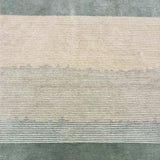 Detail of a handknotted rug with a subtle ombré effect from cream to sage green, with sage green borders