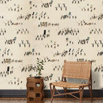 A woven chair and end table in front of a wall papered in a pattern of Japanese soldiers and horses carrying spears and flags.