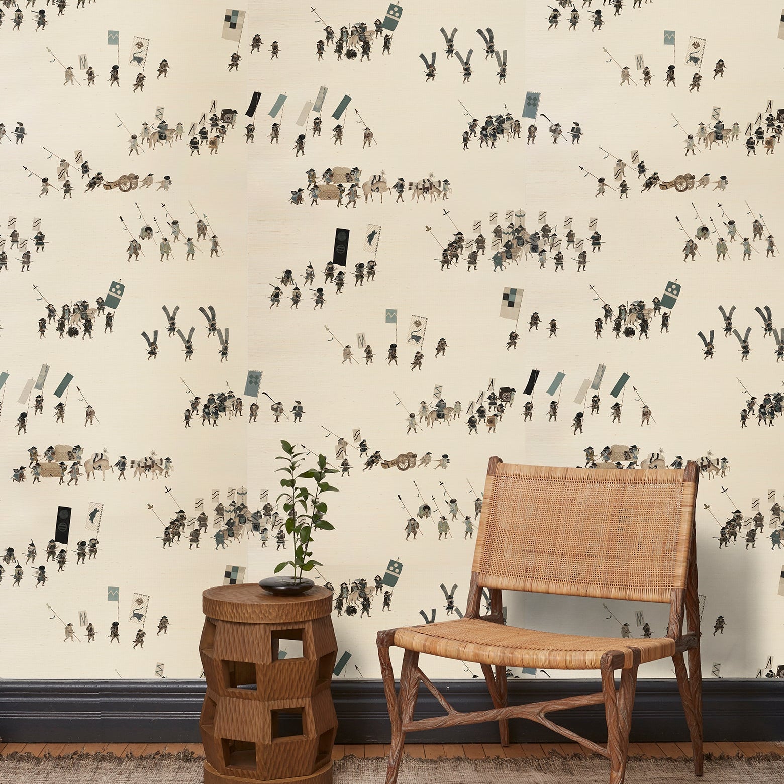 A woven chair and end table in front of a wall papered in a pattern of Japanese soldiers and horses carrying spears and flags.