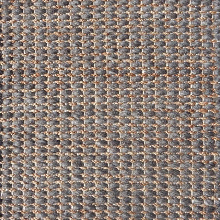 Detail of a textural rug in natural fiber and grey yarn.