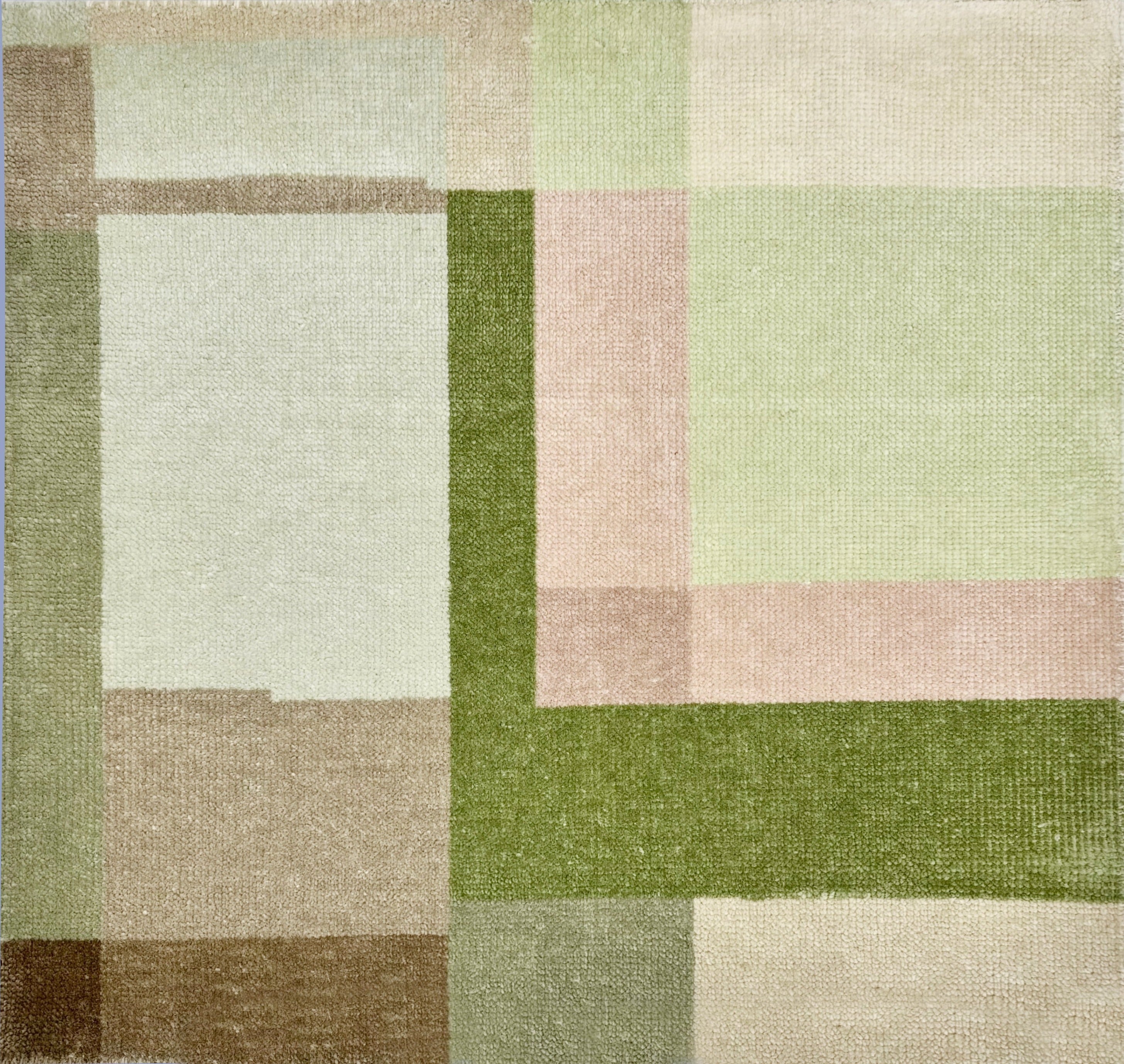 Detail of a handknotted rug in a graphic geometric design in layered shades of a green, taupe and warm pink.