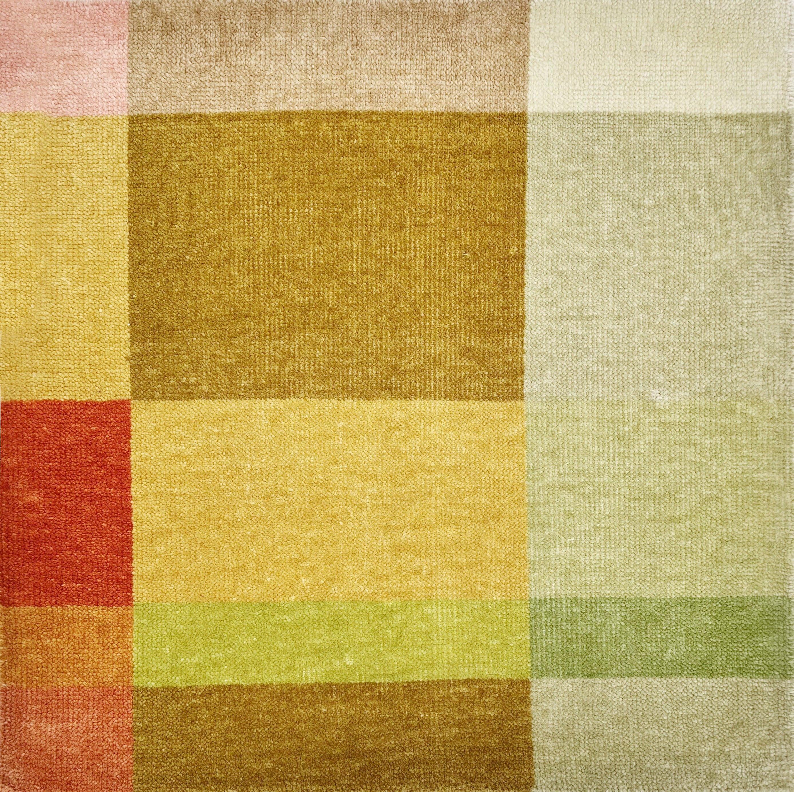 Detail of a handknotted rug in a graphic geometric design in layered shades of a green, tan, ochre and orange.