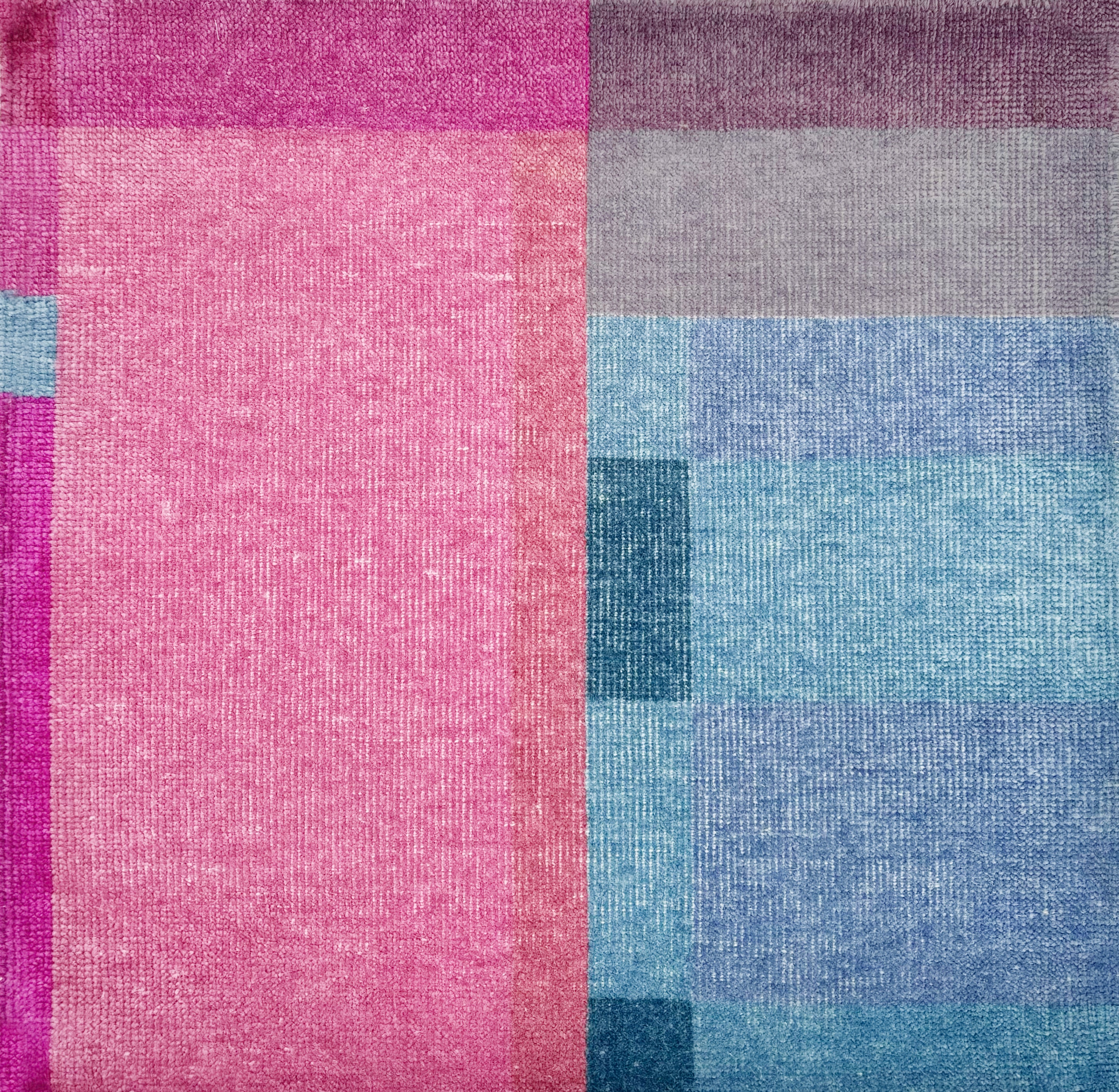 Detail of a handknotted rug in a graphic geometric design in layered shades of a fuchsia, magenta and blues.