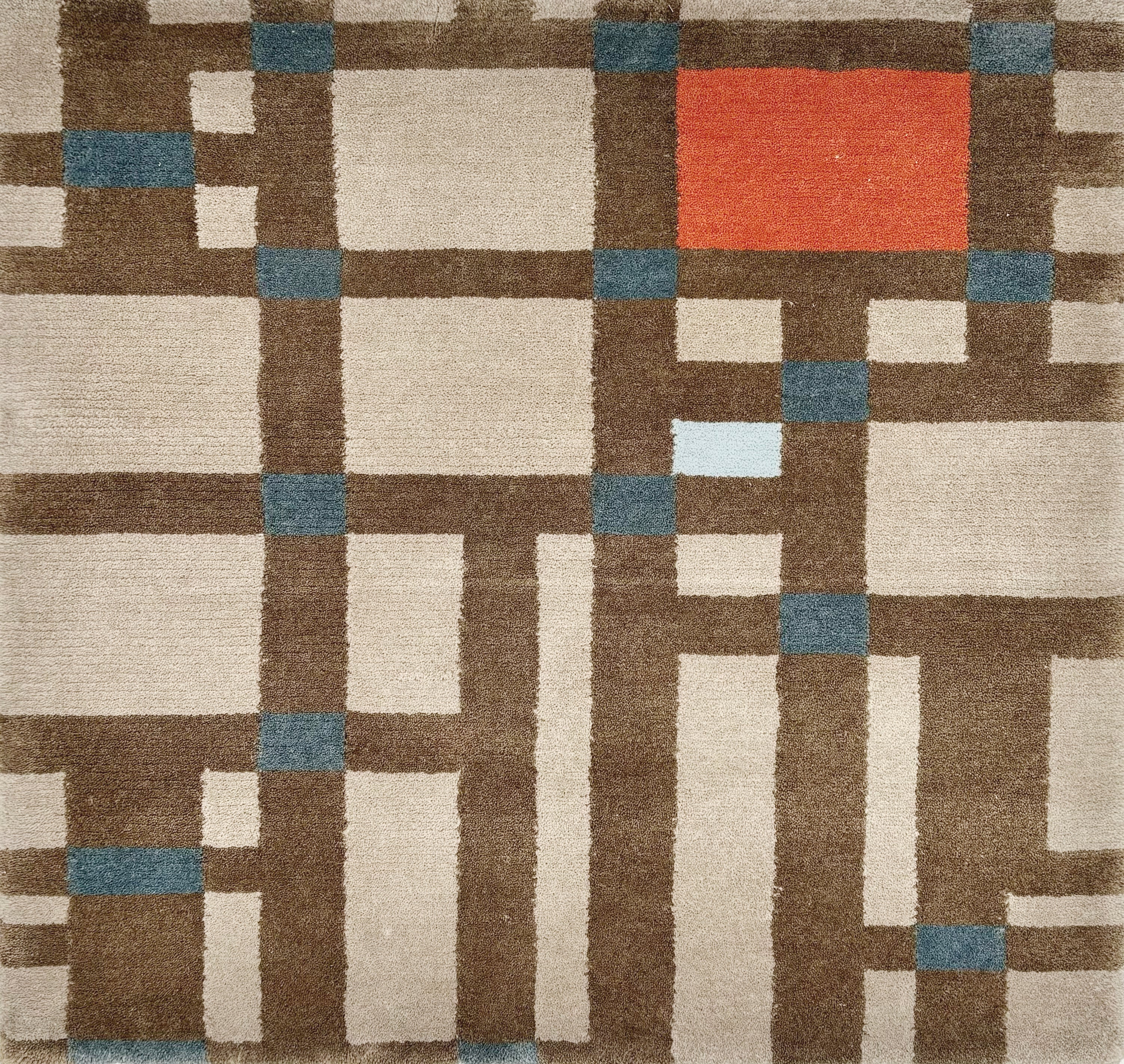 Detail of a handknotted rug in a dense geometric design in shades of brown with accents of red and blue.