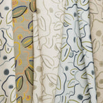 A row of fabric swatches, all in the same large-scale minimal floral print in different colorways with tan, cream and white fields.