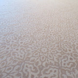 A close-up of a light beige and off-white patterned carpet with an intricate repeating damask medallion design.