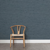 A wooden chair stands in front of a wall papered in a textural striped pattern in shades of blue and navy.