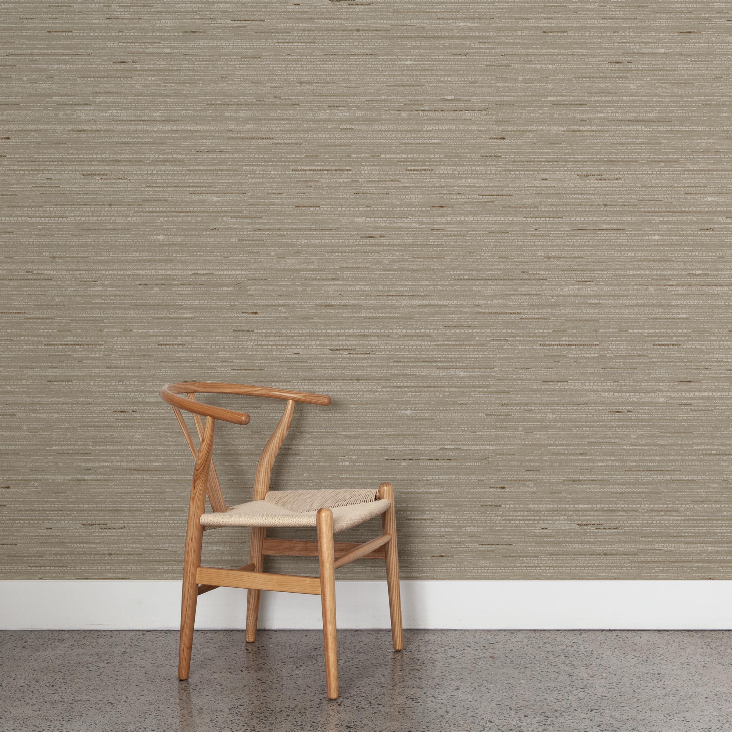 A wooden chair stands in front of a wall papered in a textural striped pattern in shades of tan and brown.