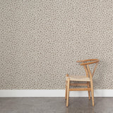 A wooden chair stands in front of a wall papered in a painterly animal print in white and brown on a sable field.