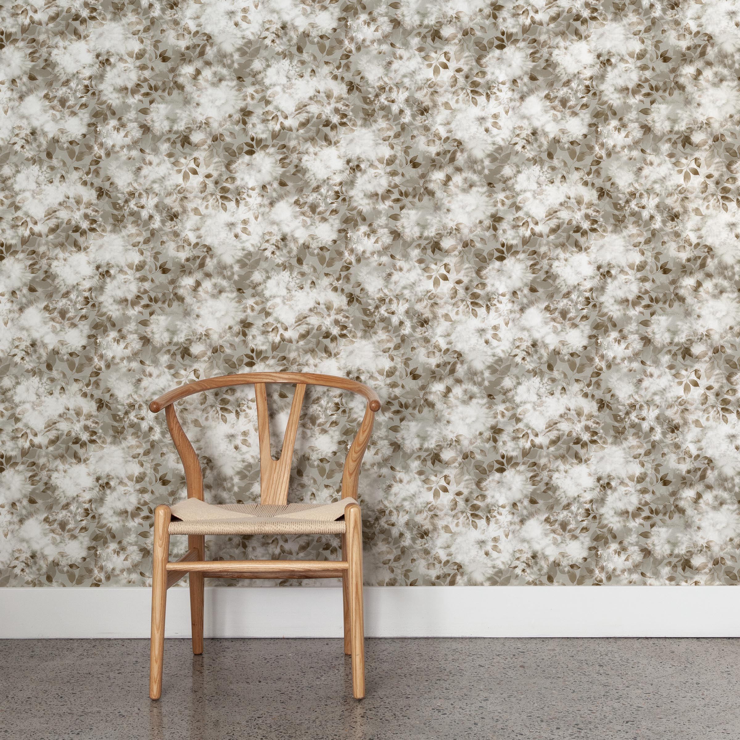 A wooden chair stands in front of a wall papered in a leaf print in shades of brown and tan with a mottled white overlay.
