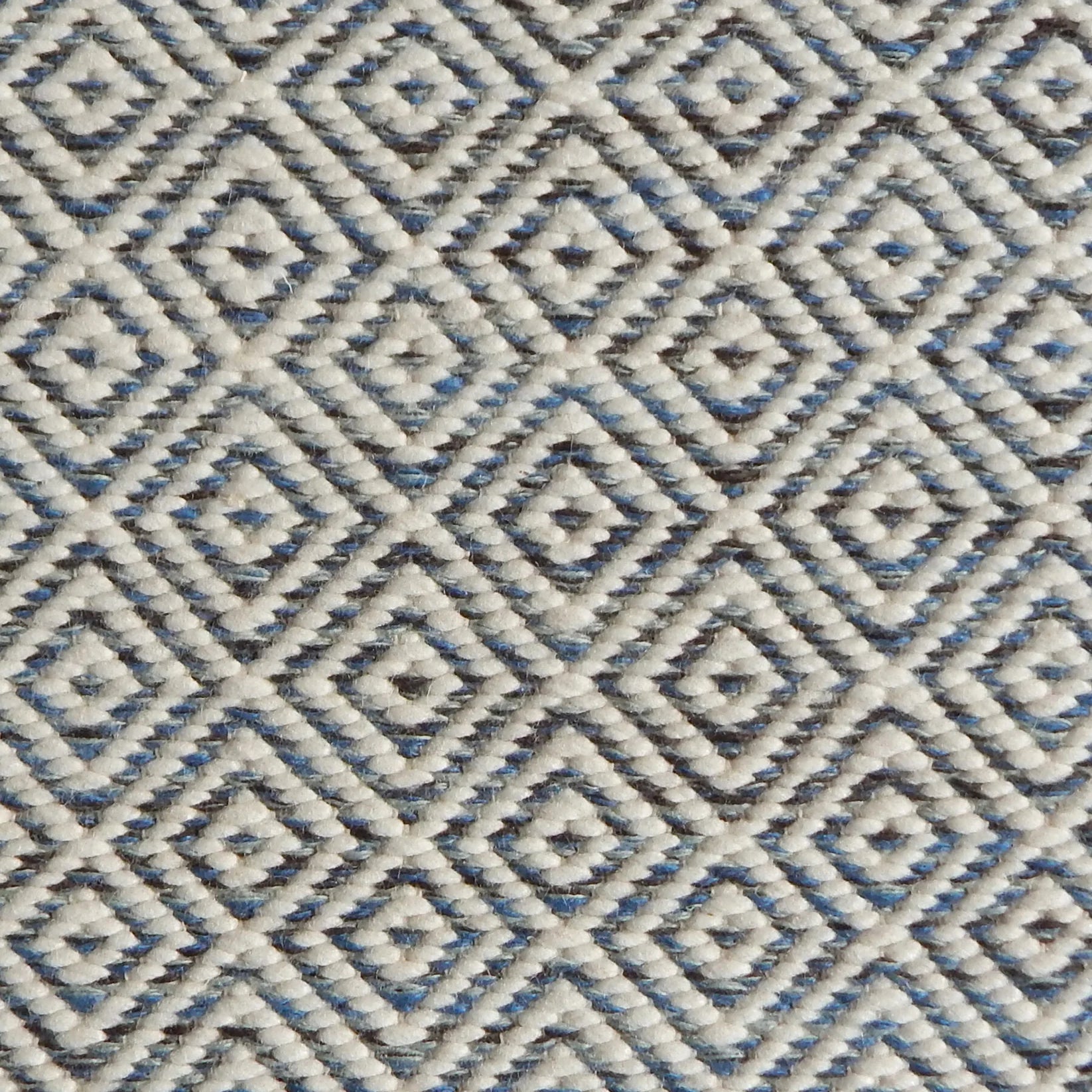 Detail of handwoven rug with diamond pattern in cream and shades of blue and brown.