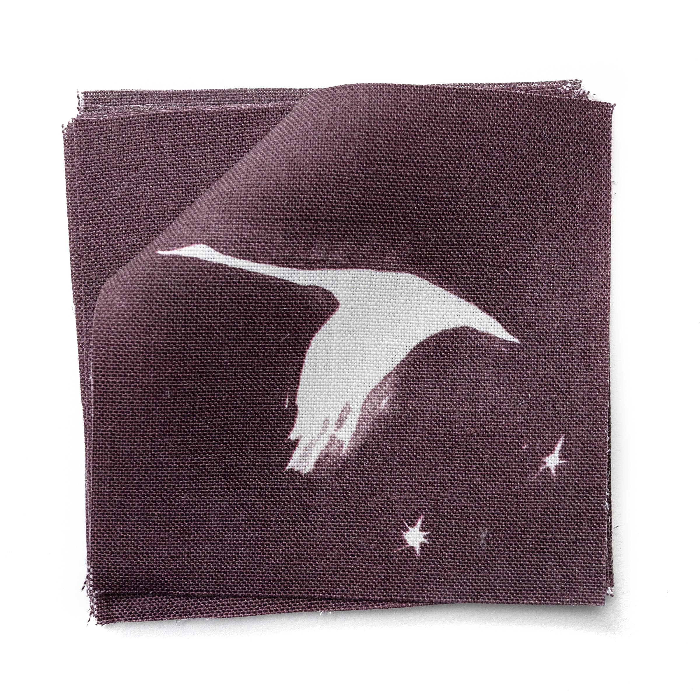 Fabric swatches in a flying geese and star pattern in white on a deep eggplant purple watercolor field.