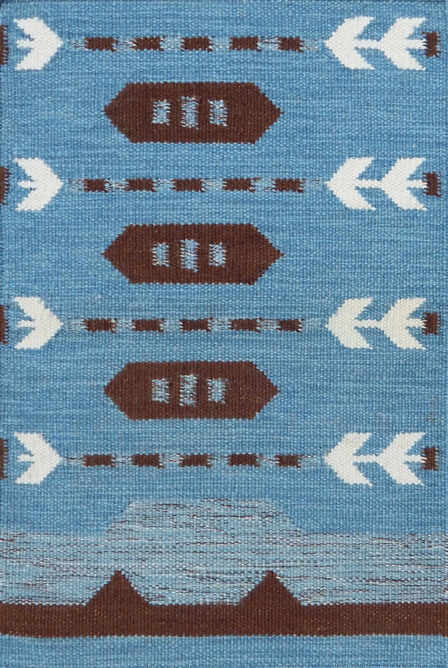 Handwoven rug detail in a Swedish arrow design in brown and white on a green field. 