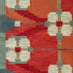 Handwoven rug detail in a Swedish Floral Trellis design in white and teal on an orange and red field