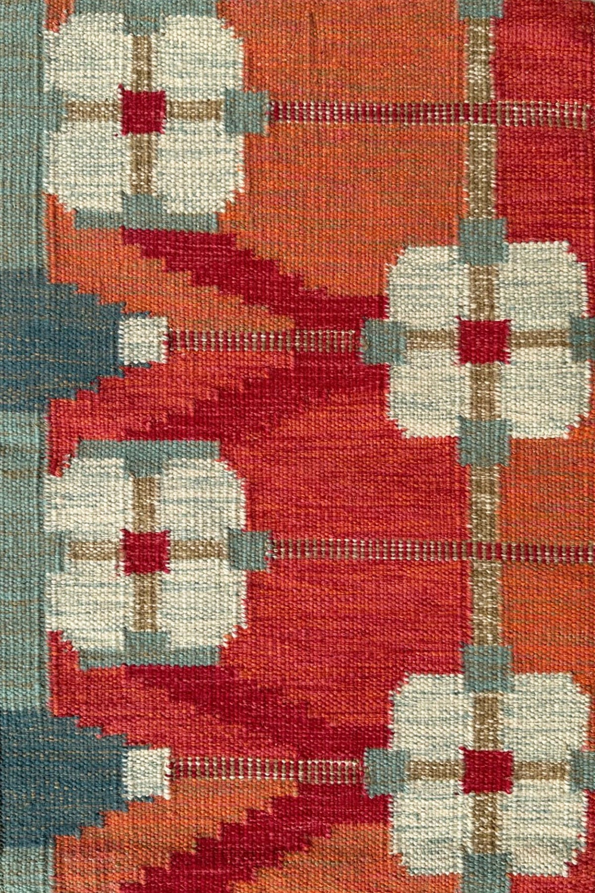 Handwoven rug detail in a Swedish Floral Trellis design in white and teal on an orange and red field