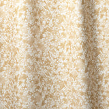 Draped fabric in a painterly branch print in white on a warm yellow watercolor field.