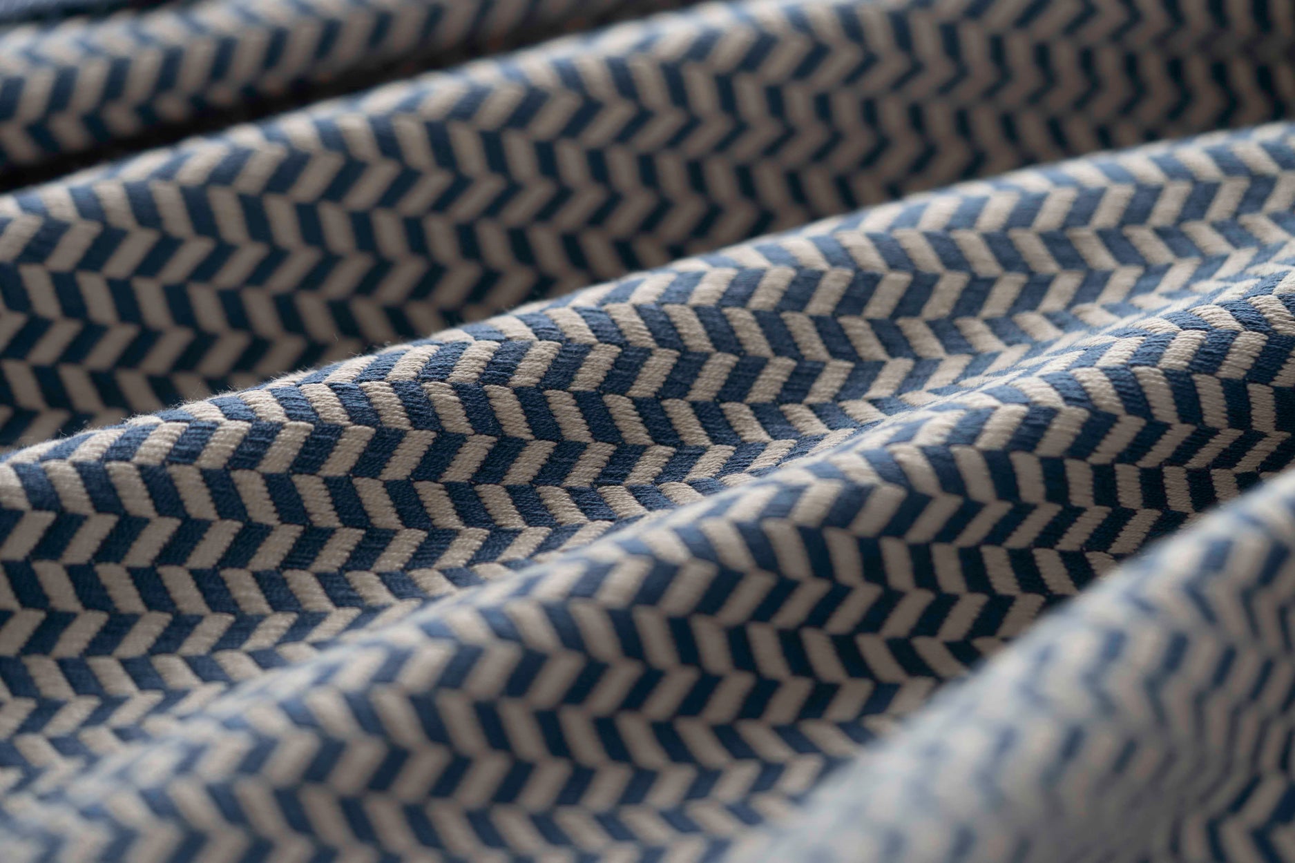 Close-up of blue and cream textured fabric with a herringbone pattern light folded. 