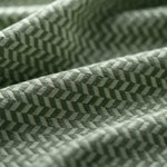 Close-up of a green textured fabric with a herringbone pattern light folded. 