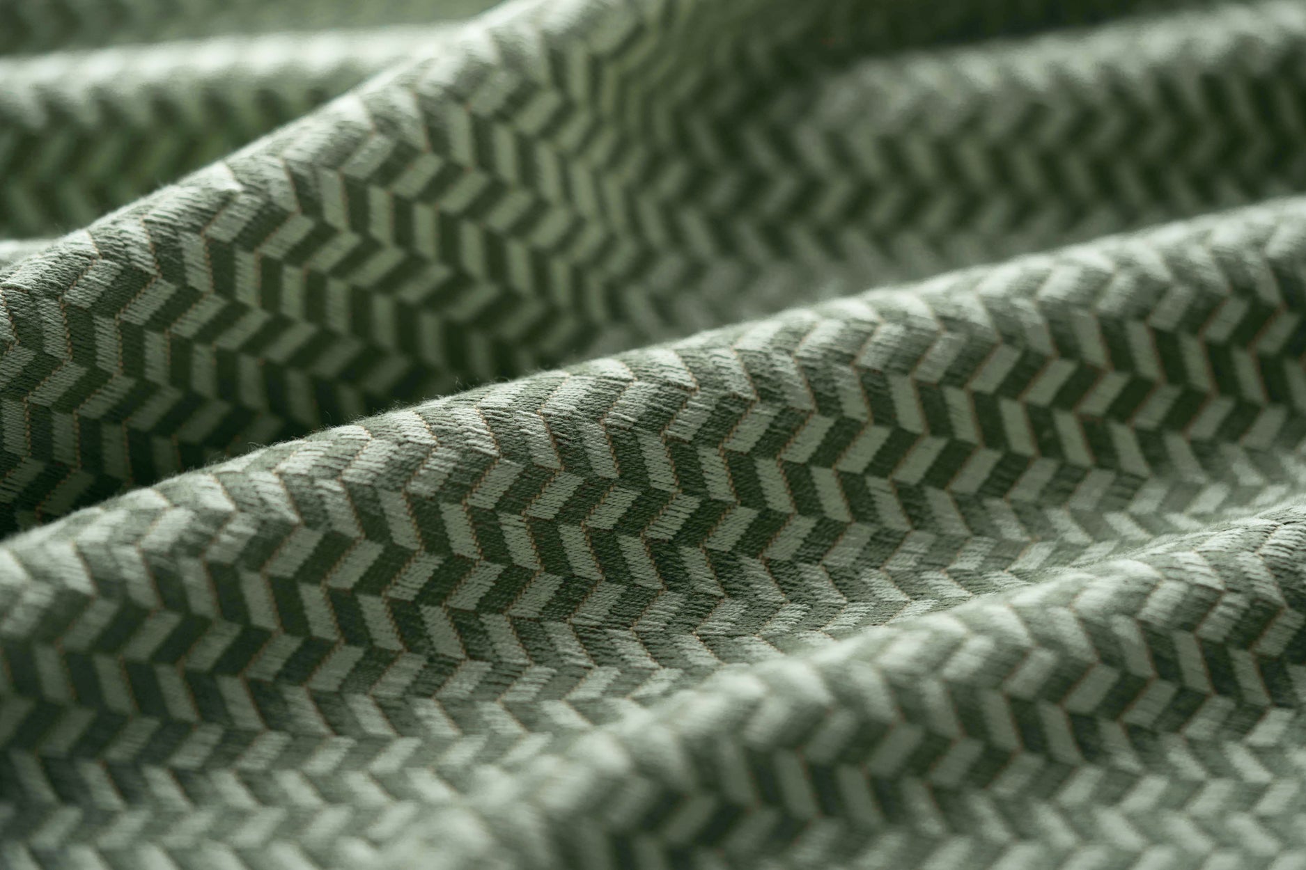 Close-up of a green textured fabric with a herringbone pattern light folded. 