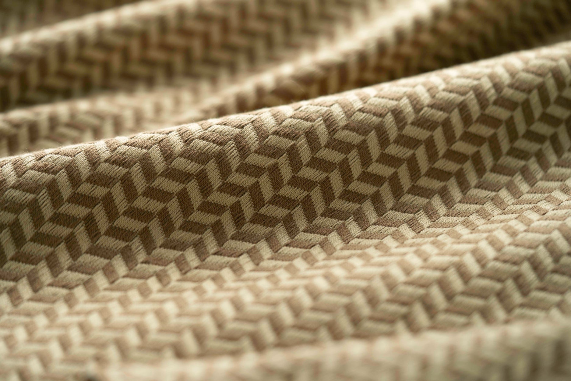 Close-up of a taupe textured fabric with a herringbone pattern light folded. 