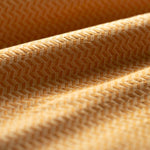 Close-up of a tan textured fabric with a herringbone pattern light folded. 