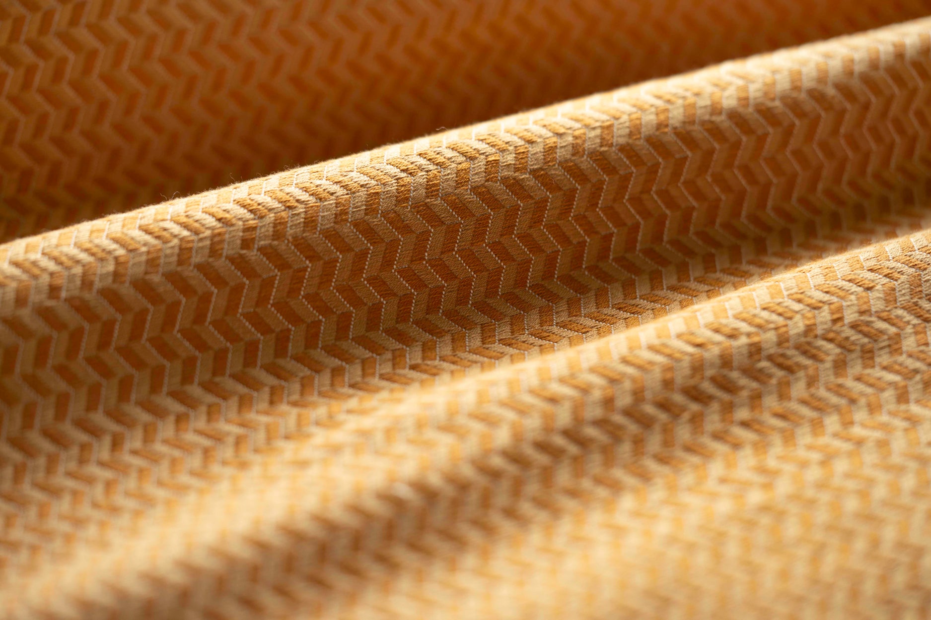Close-up of a tan textured fabric with a herringbone pattern light folded. 